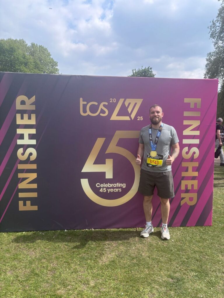 Man finished london marathon and posing for picture with medal in front of finisher backdrop